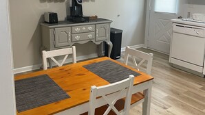 En matplats med ett träbord och vita stolar, en kaffebryggare och ett litet skåp med köksredskap.