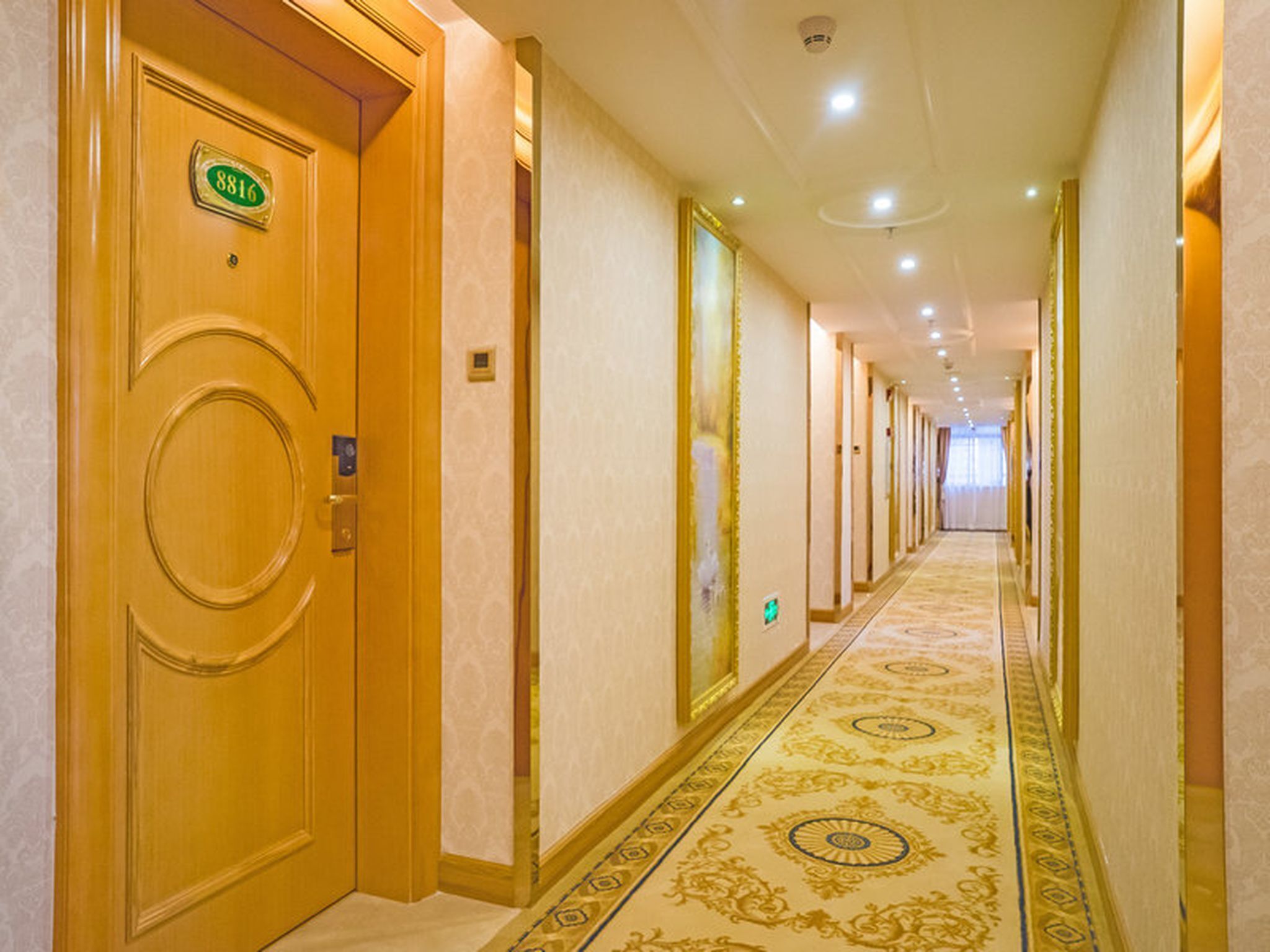 A hotel hallway with a carpeted floor, wooden doors, and a number sign above one door.