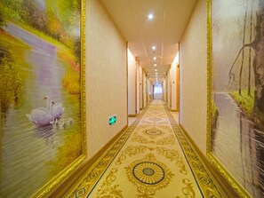 Un pasillo de hotel con un largo corredor, alfombra decorativa y grandes murales en las paredes.
