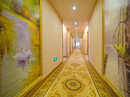 Un pasillo de hotel con un largo corredor, alfombra decorativa y grandes murales en las paredes.