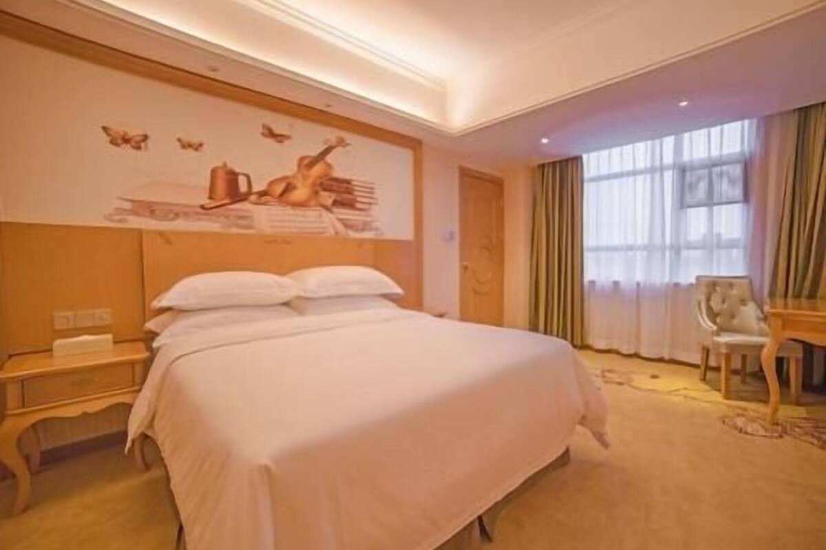 Une chambre d’hôtel avec un grand lit, une table de chevet, un bureau, une chaise et une fenêtre avec des rideaux.