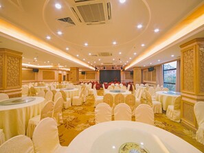 Un salón de banquetes con mesas redondas, sillas blancas y un escenario.
