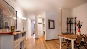 Une cuisine moderne avec un plancher en bois, un coin repas avec une table et des chaises, et un couloir menant à une autre pièce.