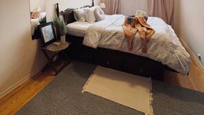 Un dormitorio con cama, mesita de noche, espejo, ventana con cortinas y una planta pequeña.