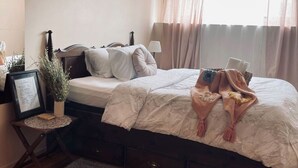 Un dormitorio ordenado con cama, mesita de noche, lámpara y una pequeña planta en maceta.