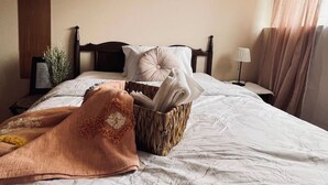 Una cama bien hecha con edredón blanco, una manta marrón y una cesta de mimbre llena de toallas dobladas.