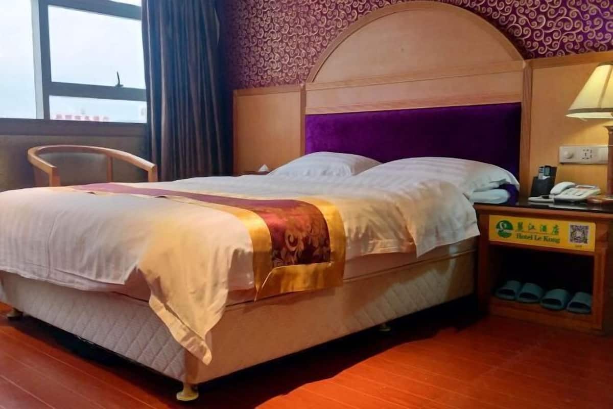 Una habitación de hotel con una cama, una silla, una mesita de noche con teléfono y un zapatero.