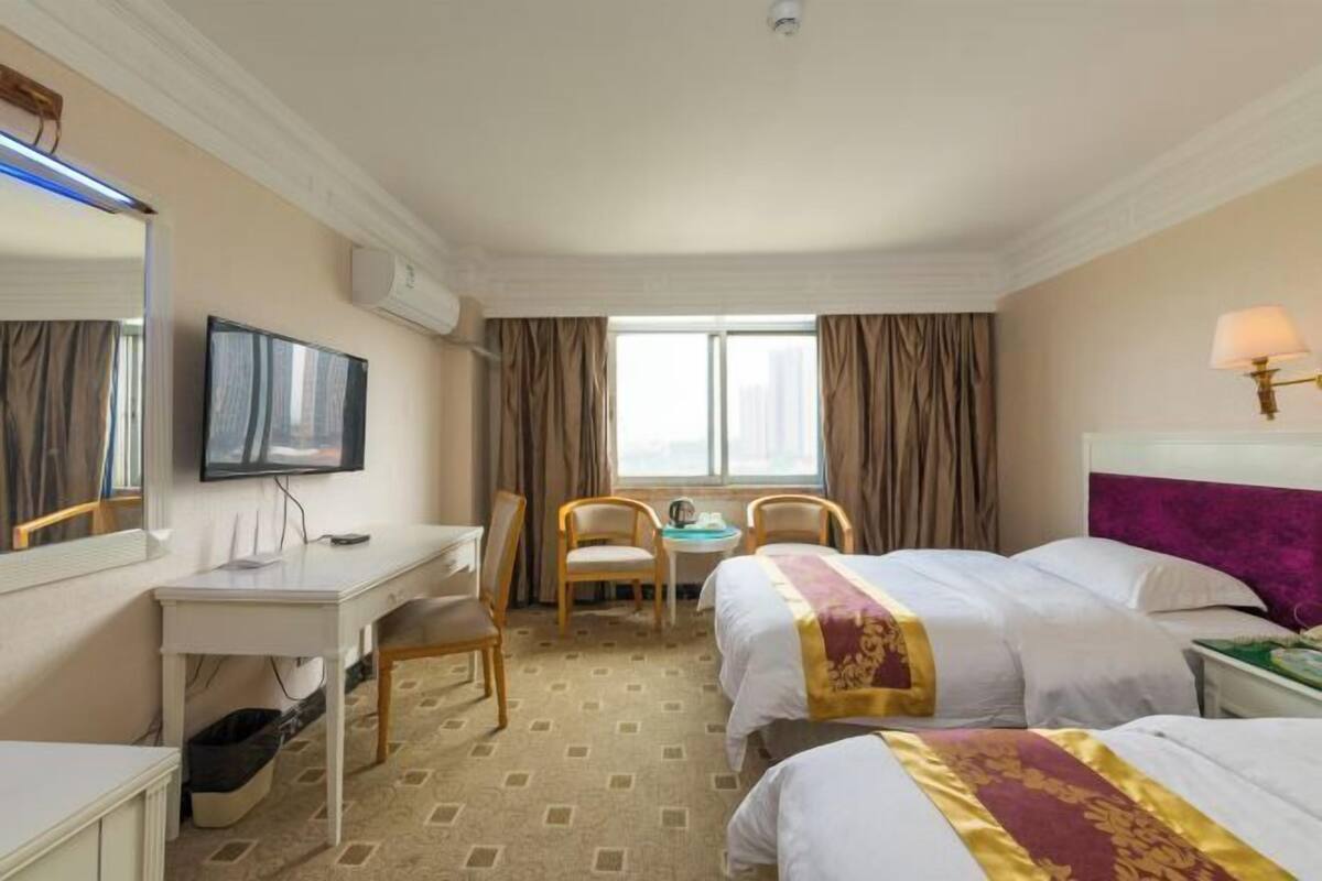Habitación de hotel con escritorio, dos camas, televisor y ventana con cortinas.