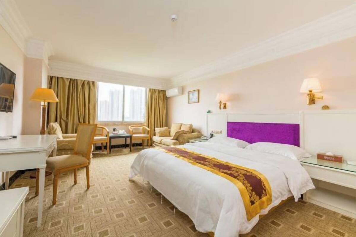 Una habitación de hotel con cama, escritorio, silla, sofá y ventana con cortinas.