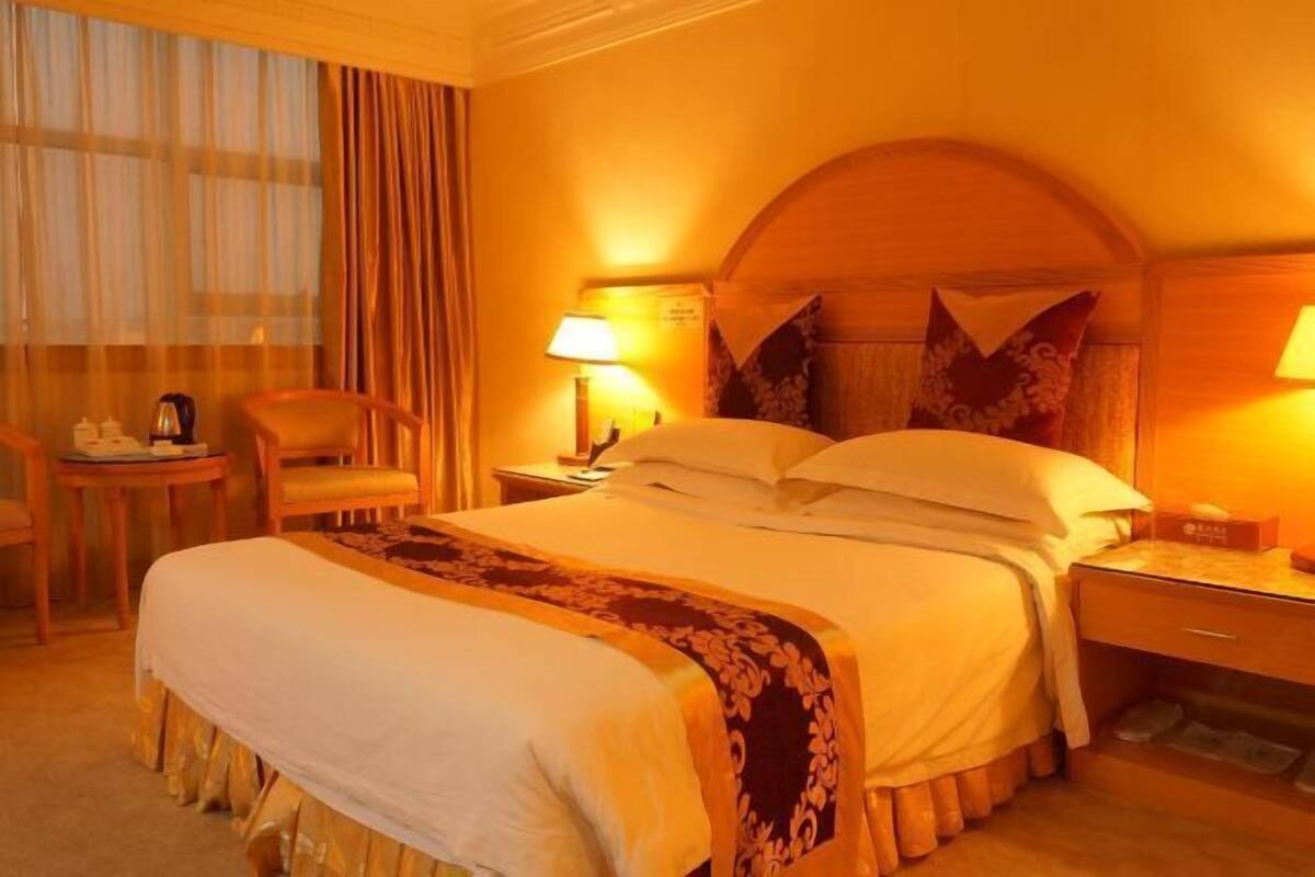 Una habitación de hotel con una cama grande, una mesita de noche, una silla y una ventana con cortinas.
