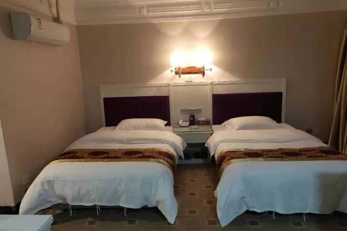 Habitación de hotel con dos camas individuales, una mesita de noche, un espejo y un equipo de aire acondicionado.