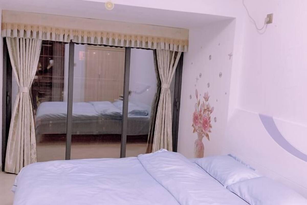A bedroom with a large bed, a sliding glass door leading to a balcony, and a wall with floral decals.