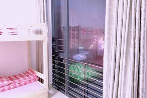 A room with a bunk bed, a sliding glass door, and a view of buildings outside. - Free Space Youth Hostel (Zhanjiang)