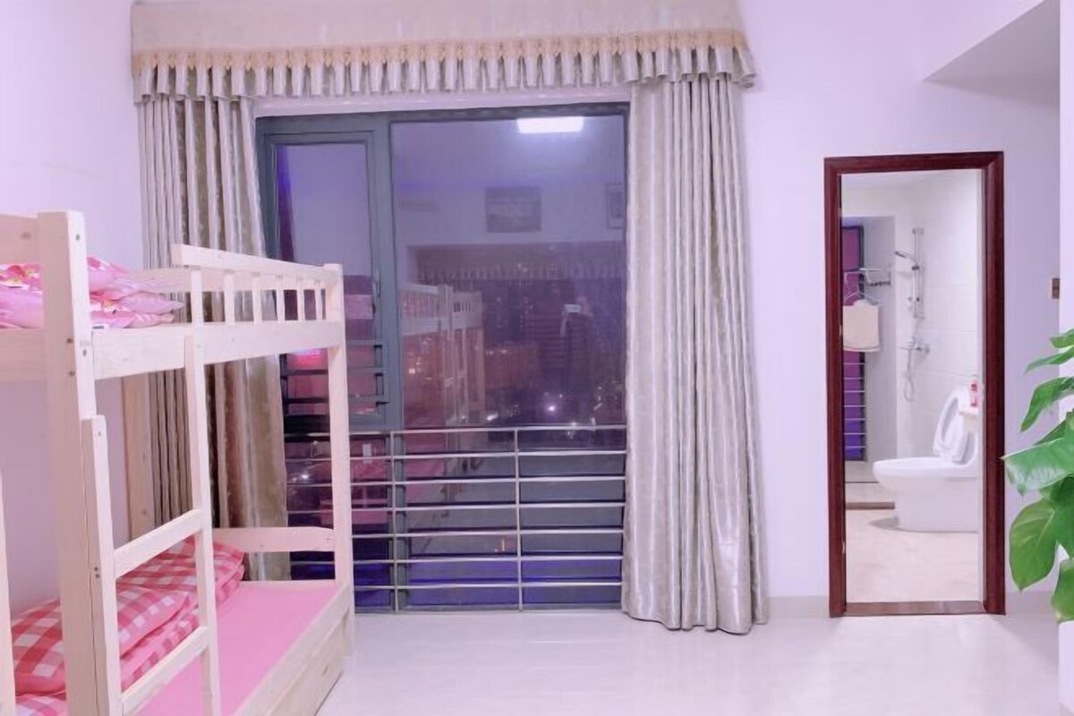 A bedroom with a bunk bed, a large window with curtains, and a bathroom visible through an open door.