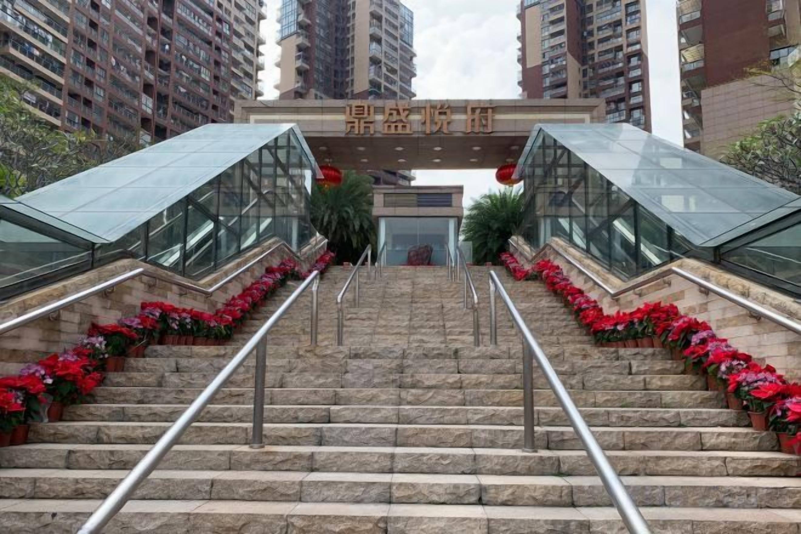 A set of stone stairs leading to a building entrance with a glass facade, surrounded by red flowers.