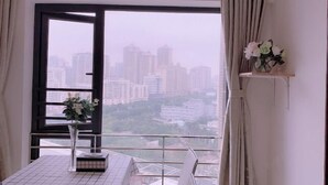 A room with a large window, a table with a vase of flowers, and a city view. - Free Space Youth Hostel (Zhanjiang)