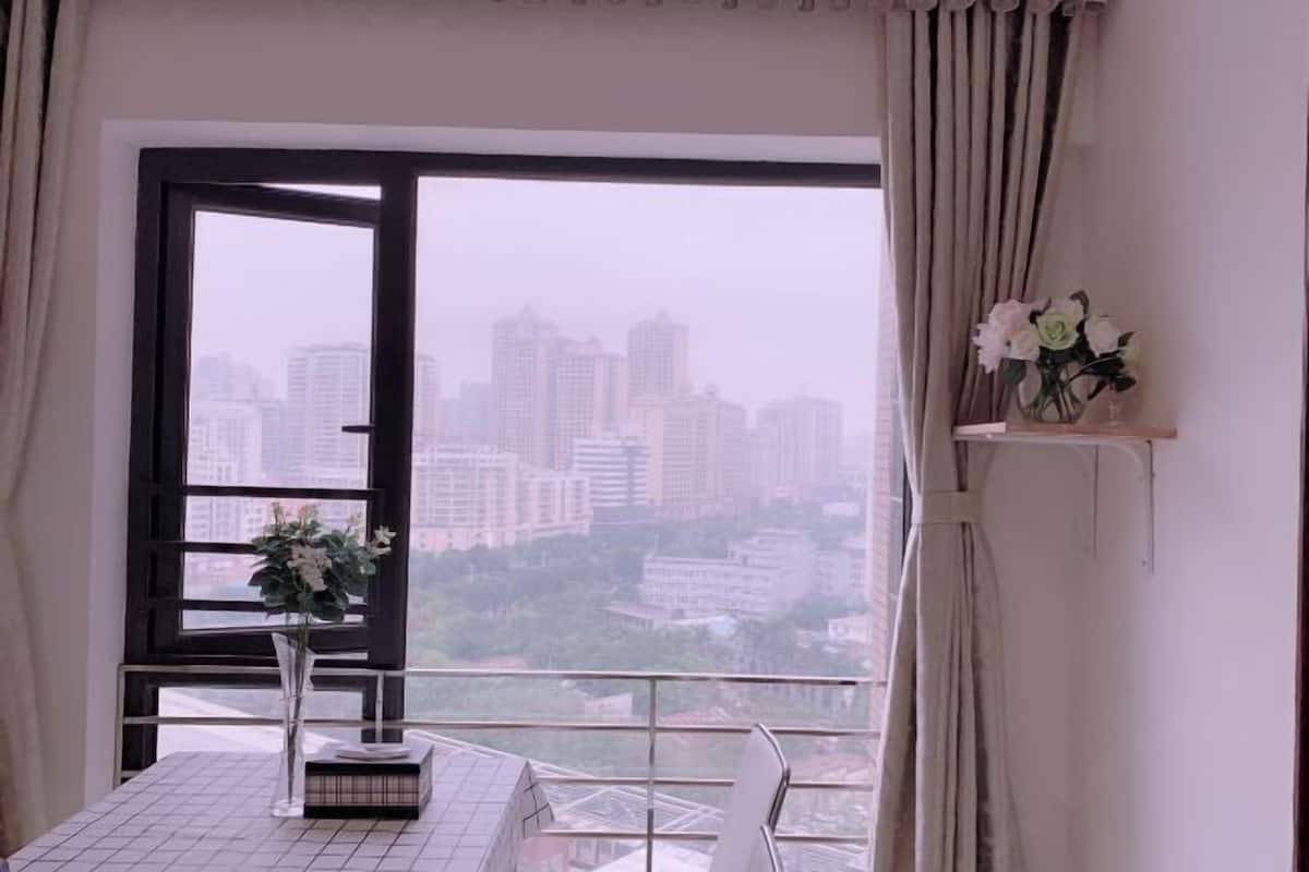 A room with a large window, a table with a vase of flowers, and a city view.