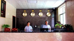 A reception desk with two staff members, a black marble wall, and a decorative green dragon statue.