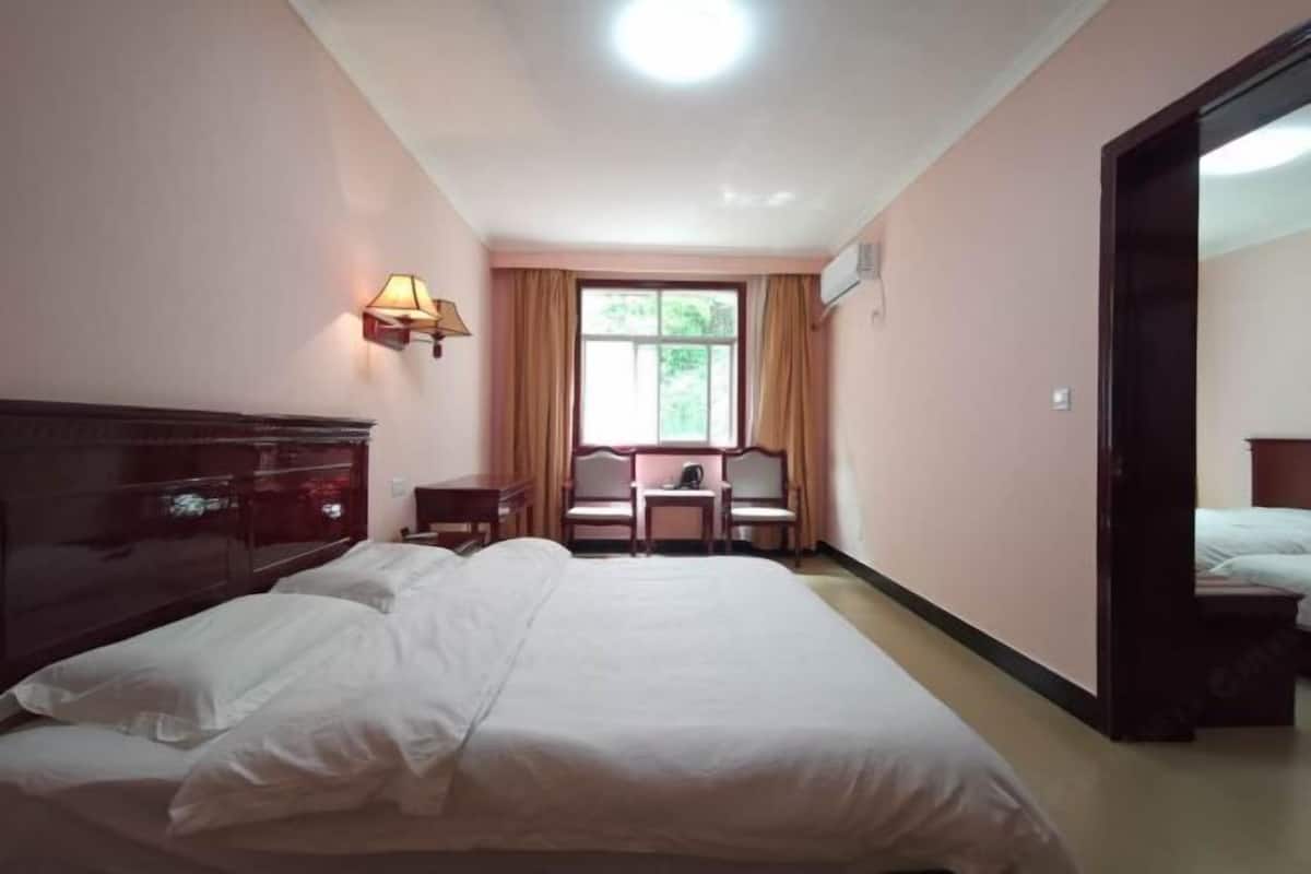 A hotel room with a large bed, a desk, a chair, and a window with curtains.