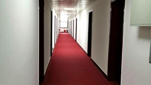 A long hallway with a red carpet, white walls, and doors on both sides.