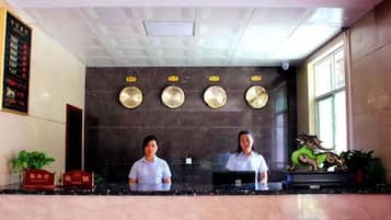 A reception desk with two staff members, a wall with decorative plates, and a window with natural light.