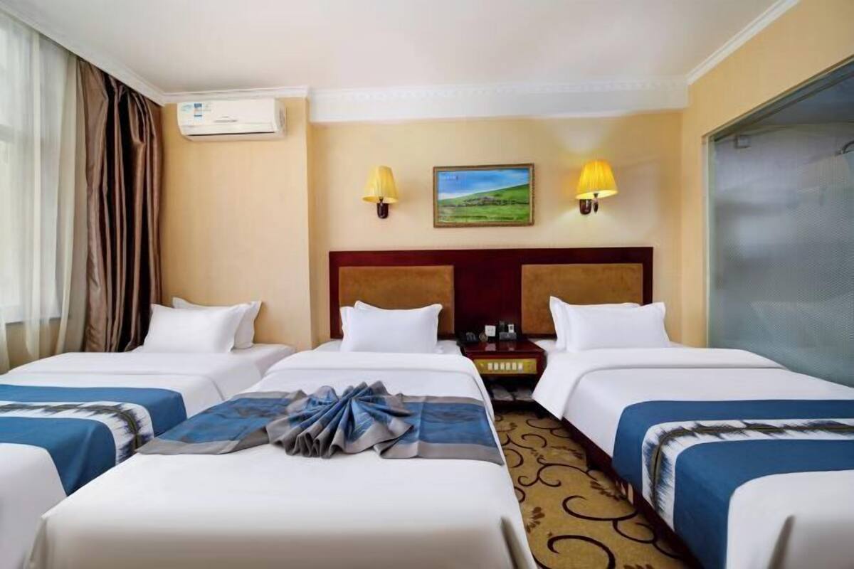 A hotel room with two beds, a headboard, a painting, two wall lamps, and an air conditioning unit.