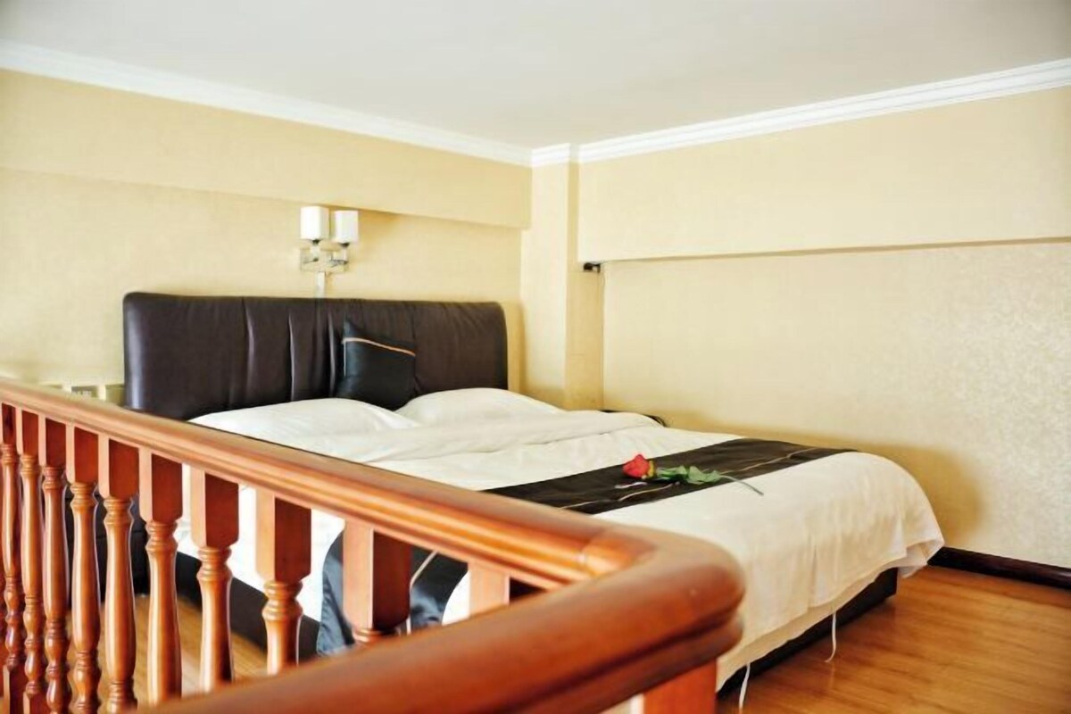A hotel room with a bed, wooden railing, and a wall-mounted light fixture.