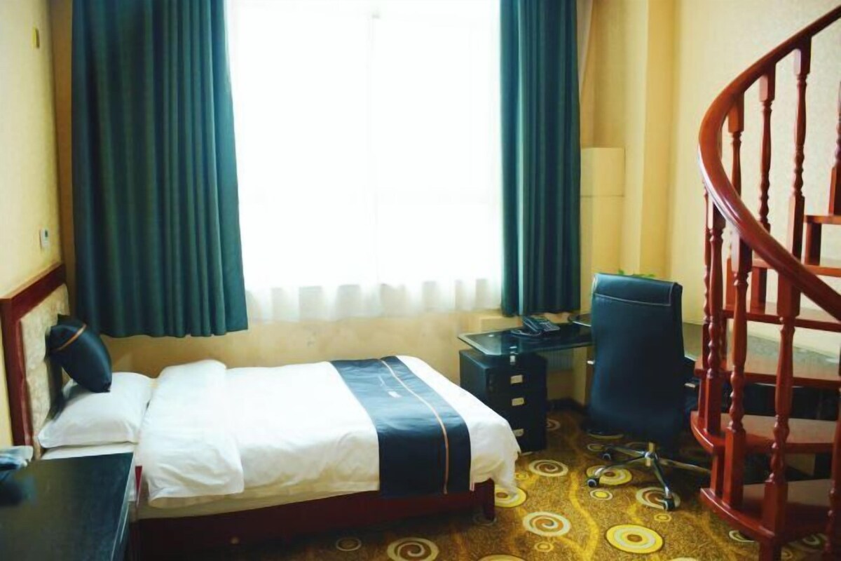 A hotel room with a bed, desk, chair, and a staircase.