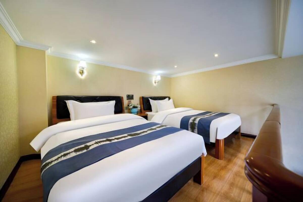 A hotel room with two beds, a wooden floor, and a ceiling light fixture.