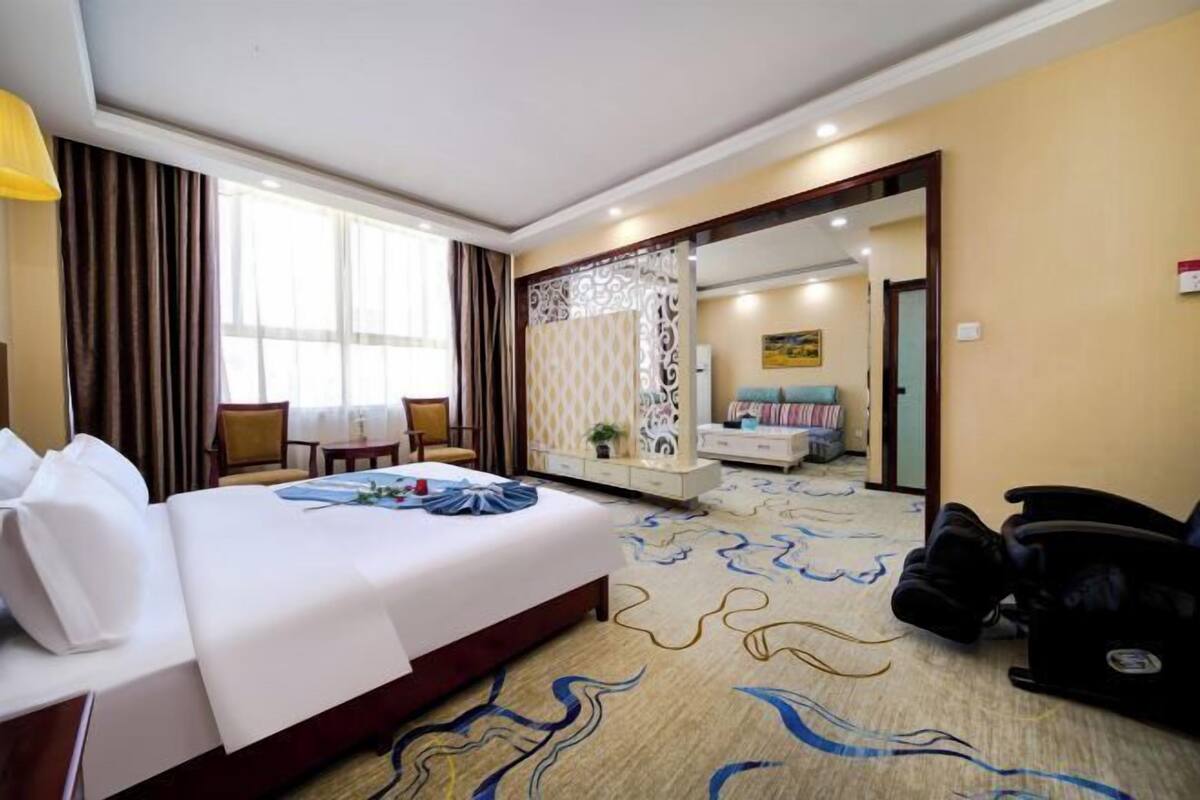 A hotel room with a bed, a desk, a chair, a sofa, and a bathroom visible through a mirror.