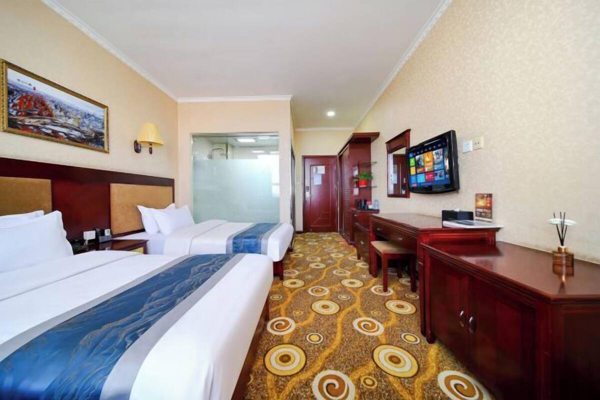 A hotel room with two beds, a desk, a chair, a television, and a patterned carpet.