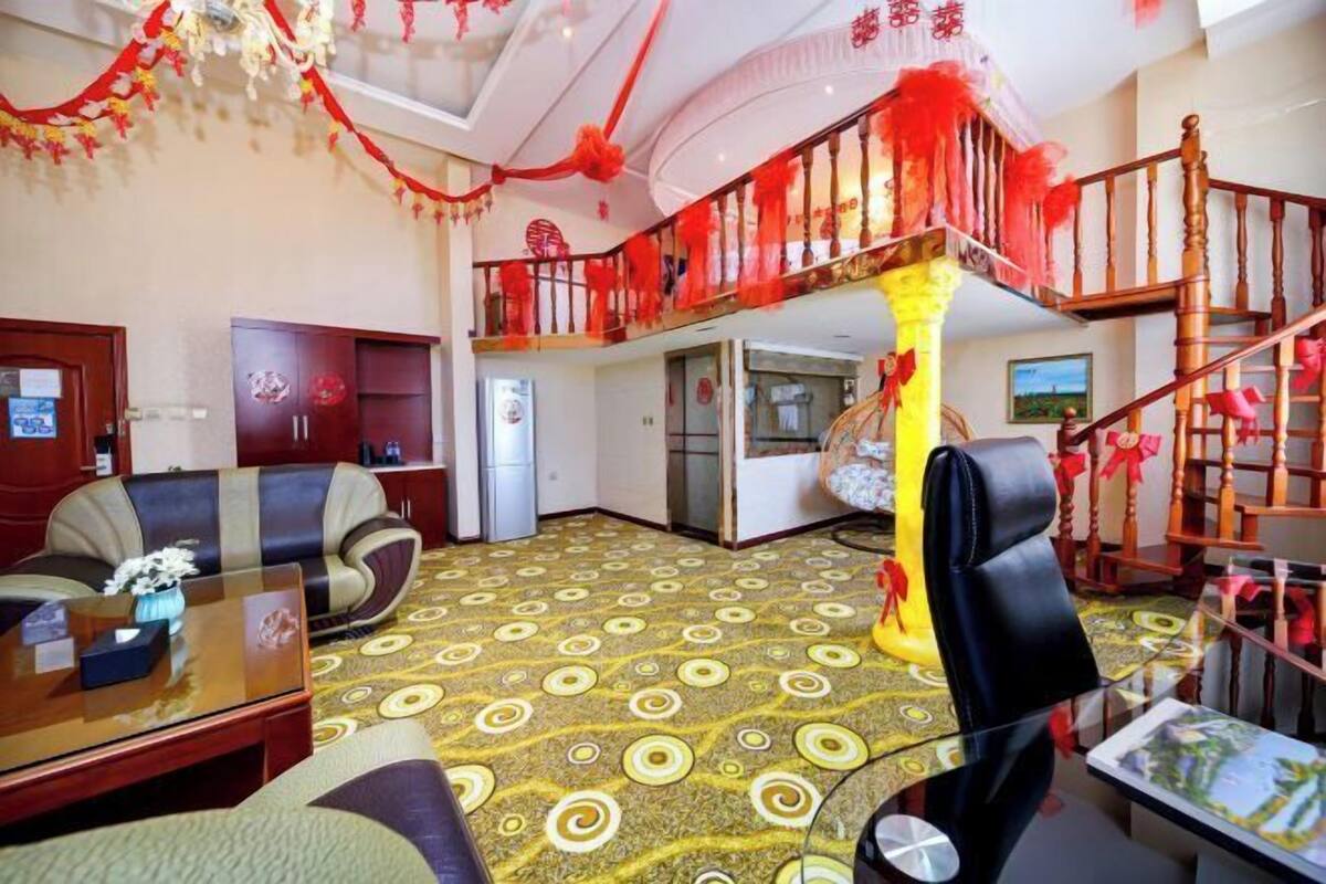 A hotel lobby with a sofa, a coffee table, a staircase with red decorations, and a patterned carpet.