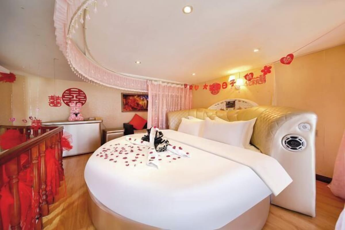 A hotel room with a bed, a bedside table, a wall decoration, and a curtain.