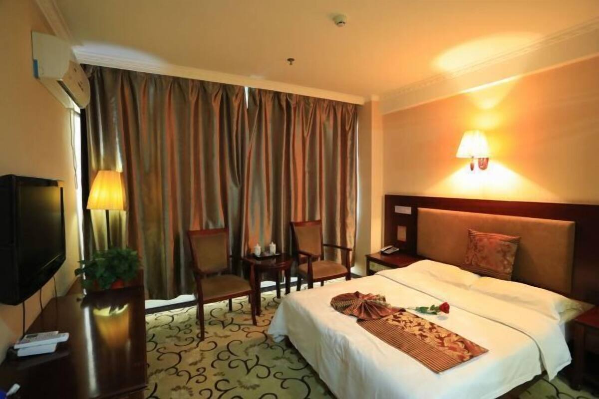 A hotel room with a bed, a desk with a lamp, a TV, and curtains.