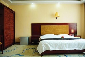 A hotel room with a large bed, a nightstand, a lamp, a wardrobe, and a trash bin.