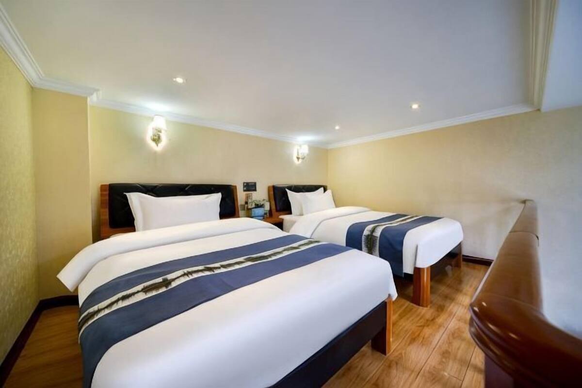 A hotel room with two beds, a wooden floor, and a nightstand with a lamp.