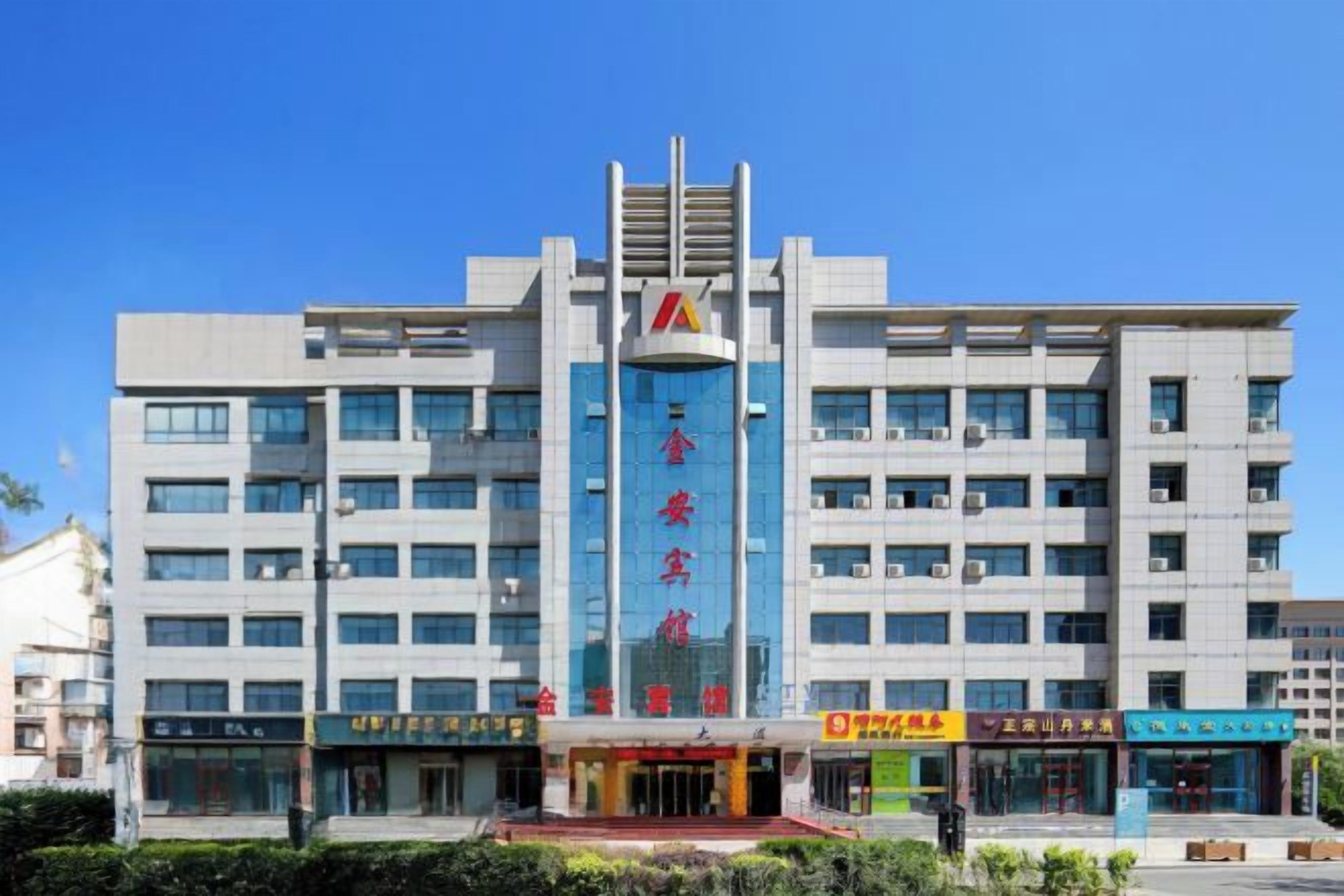 A multi-story building with a prominent vertical sign in the center, multiple ground-level commercial spaces, and a clear sky.