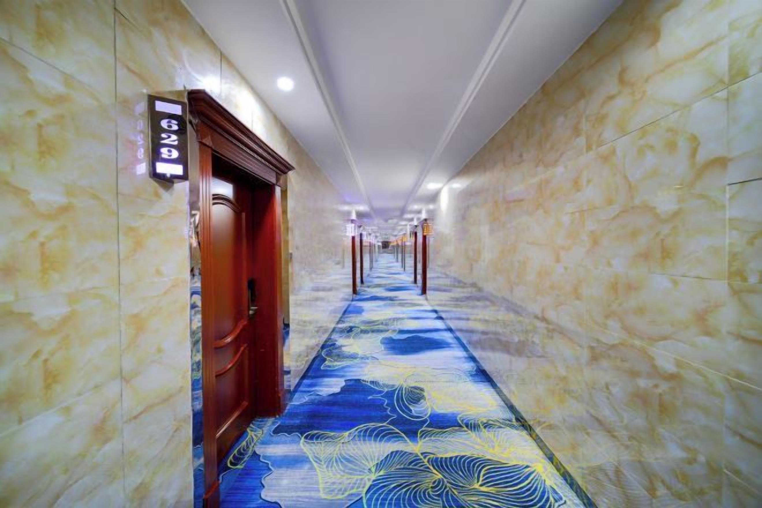 A hallway with marble walls and a patterned carpet, leading to a door with a sign above it.