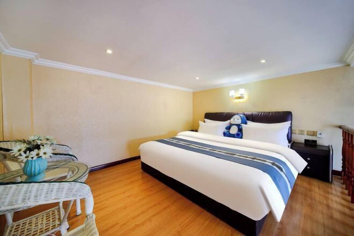A hotel room with a bed, a small table with chairs, a vase of flowers, and a nightstand.