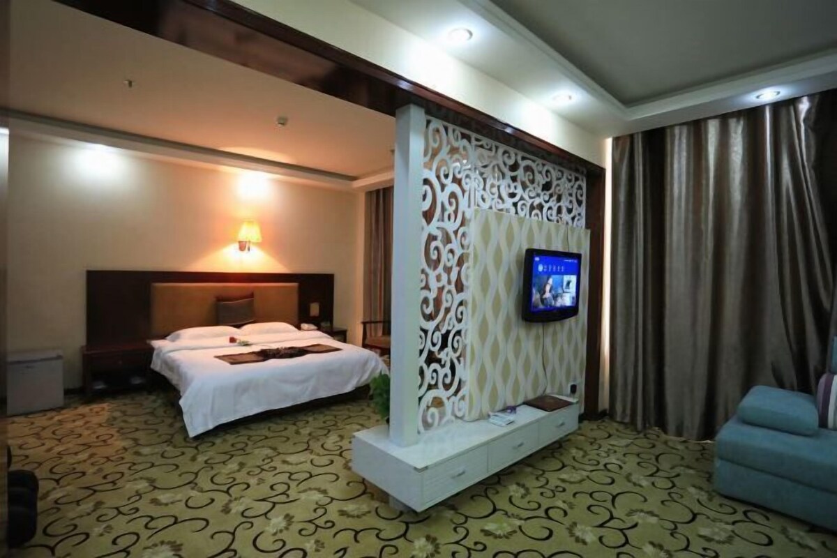 A hotel room with a bed, a TV mounted on a decorative panel, a sofa, and a patterned carpet.
