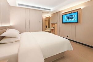 Una habitación de hotel moderna con cama, televisor montado en la pared y armario empotrado.