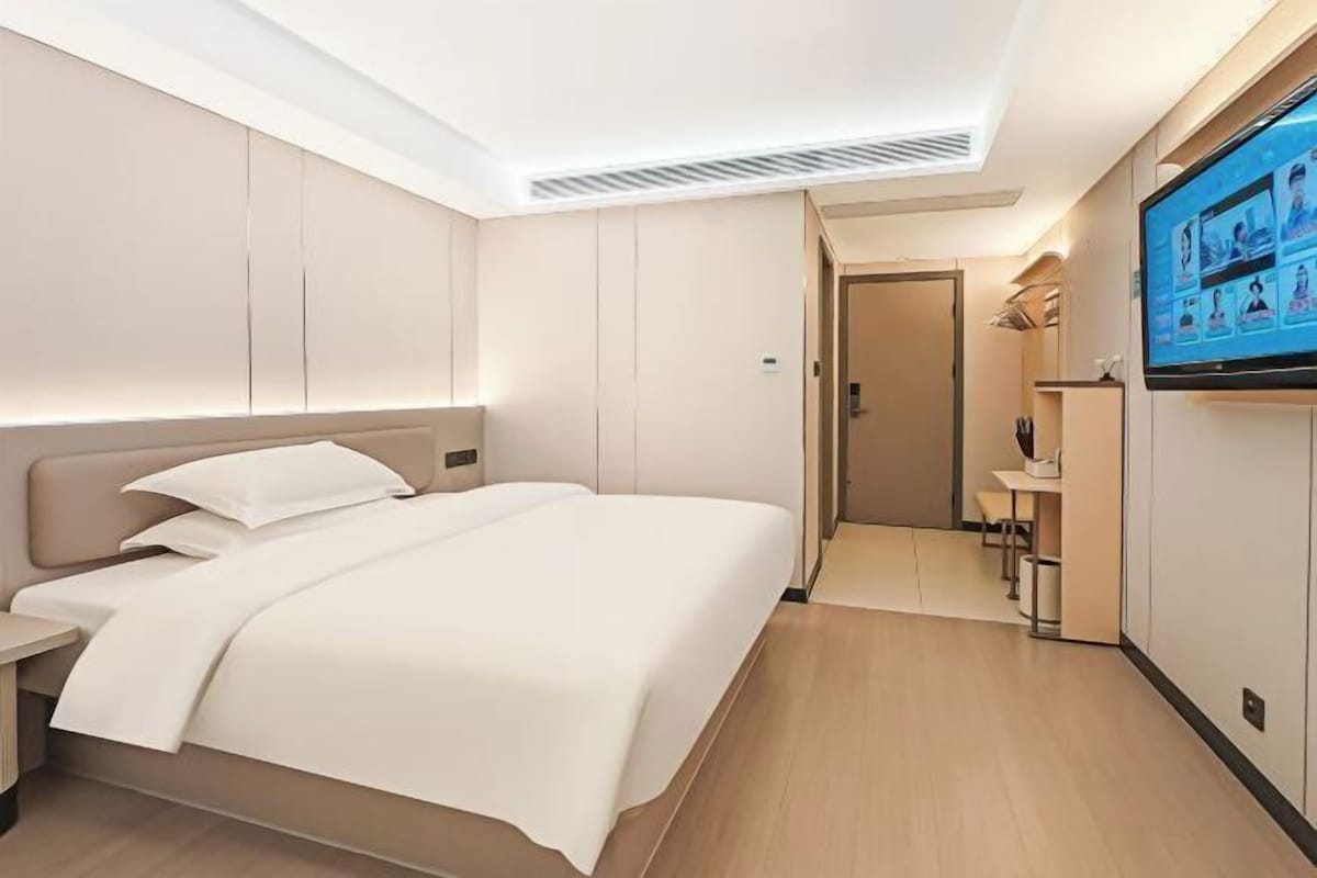 A modern hotel room with a bed, a TV, a desk, and a walk-in closet.