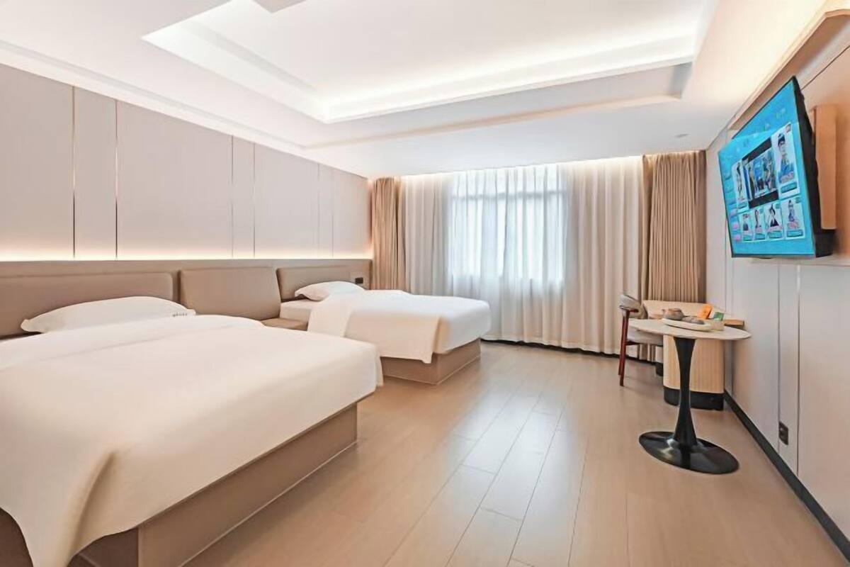 A hotel room with two beds, a TV, a small table, and a window with curtains.