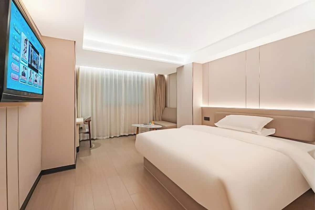 A hotel room with a large bed, a TV mounted on the wall, a small table, and a chair.