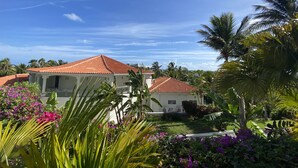 A white building with a red-tiled roof, surrounded by lush greenery and purple flowers.