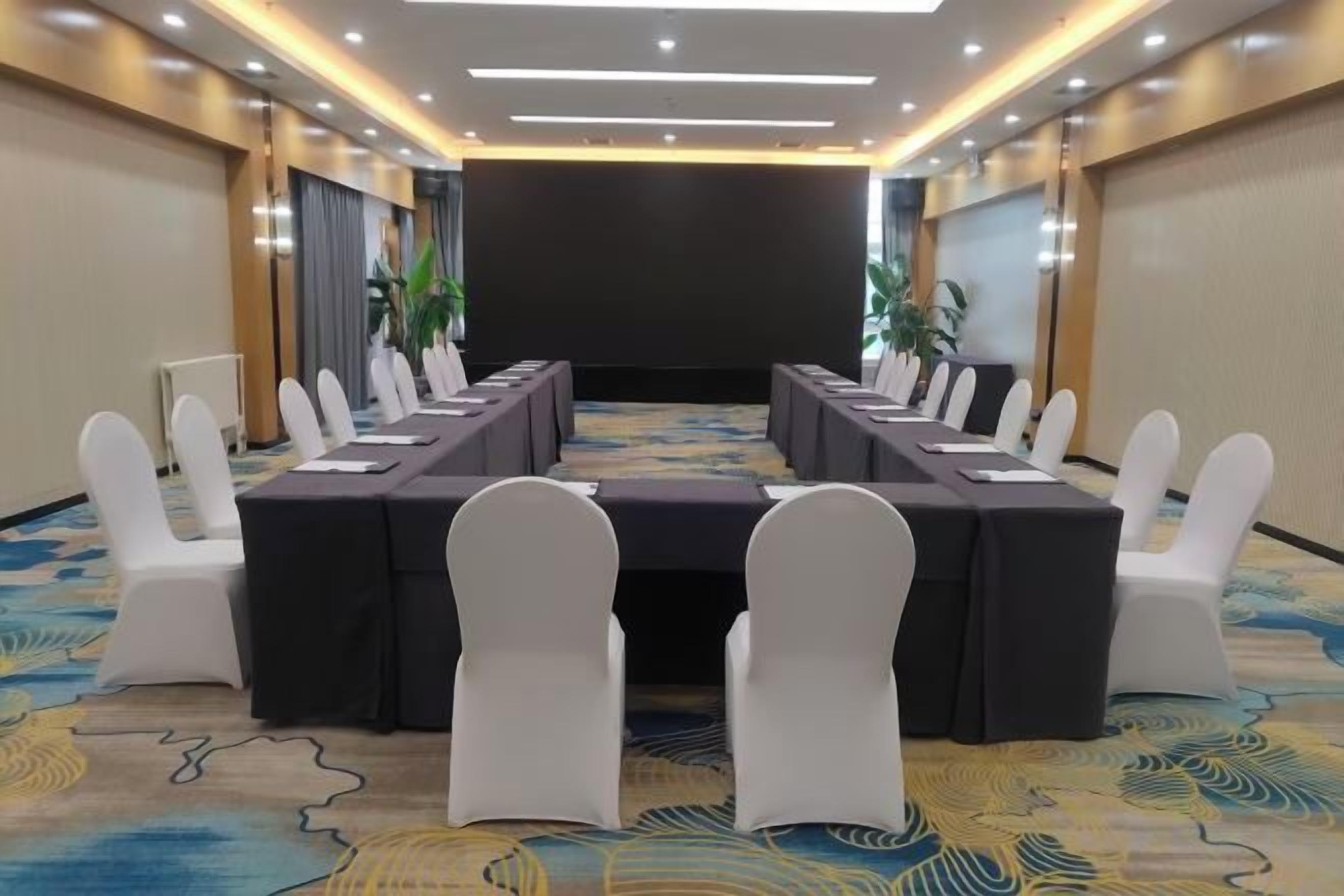 A conference room with a long table, white chairs, and a carpeted floor.