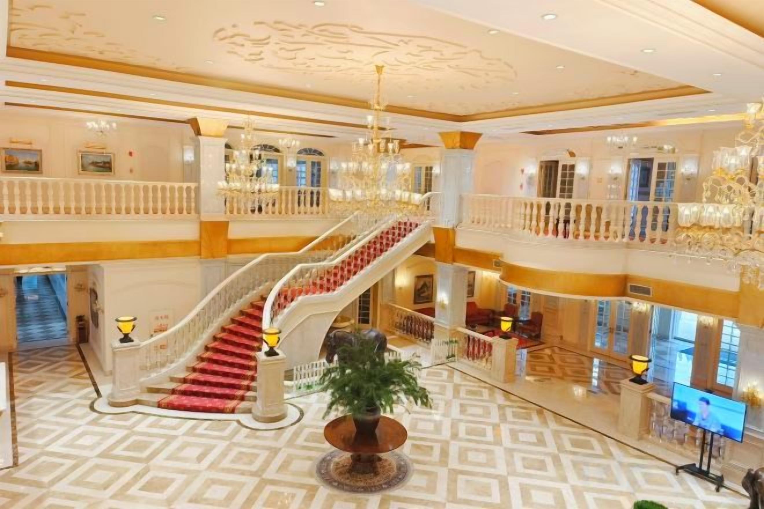 Un hall d’hôtel à plusieurs niveaux, doté d’un grand escalier, d’une plante centrale et d’un lustre.