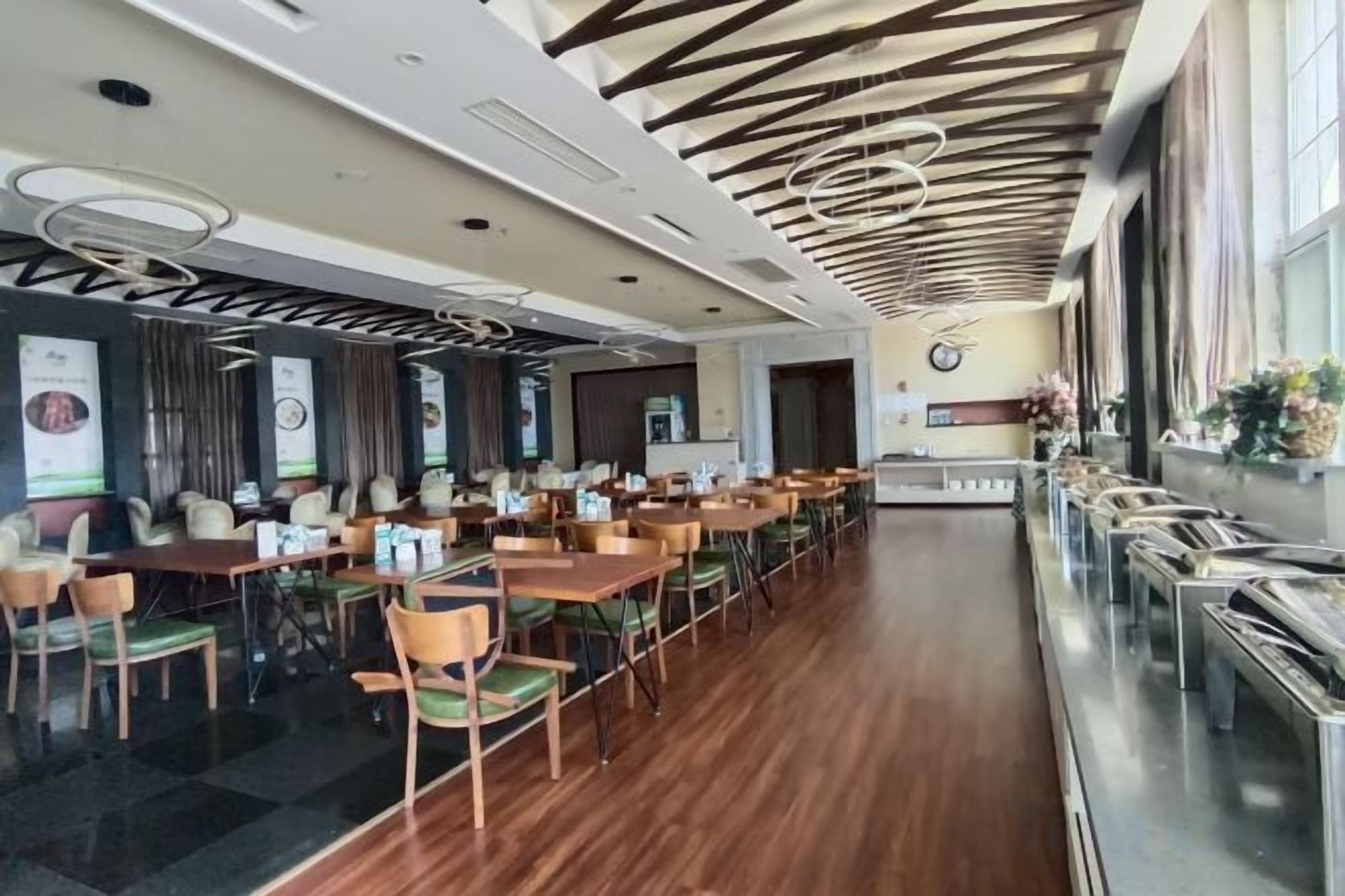 Un'ampia sala da pranzo con lunghe tavolate e sedie, un moderno design del soffitto e vista sull'esterno.