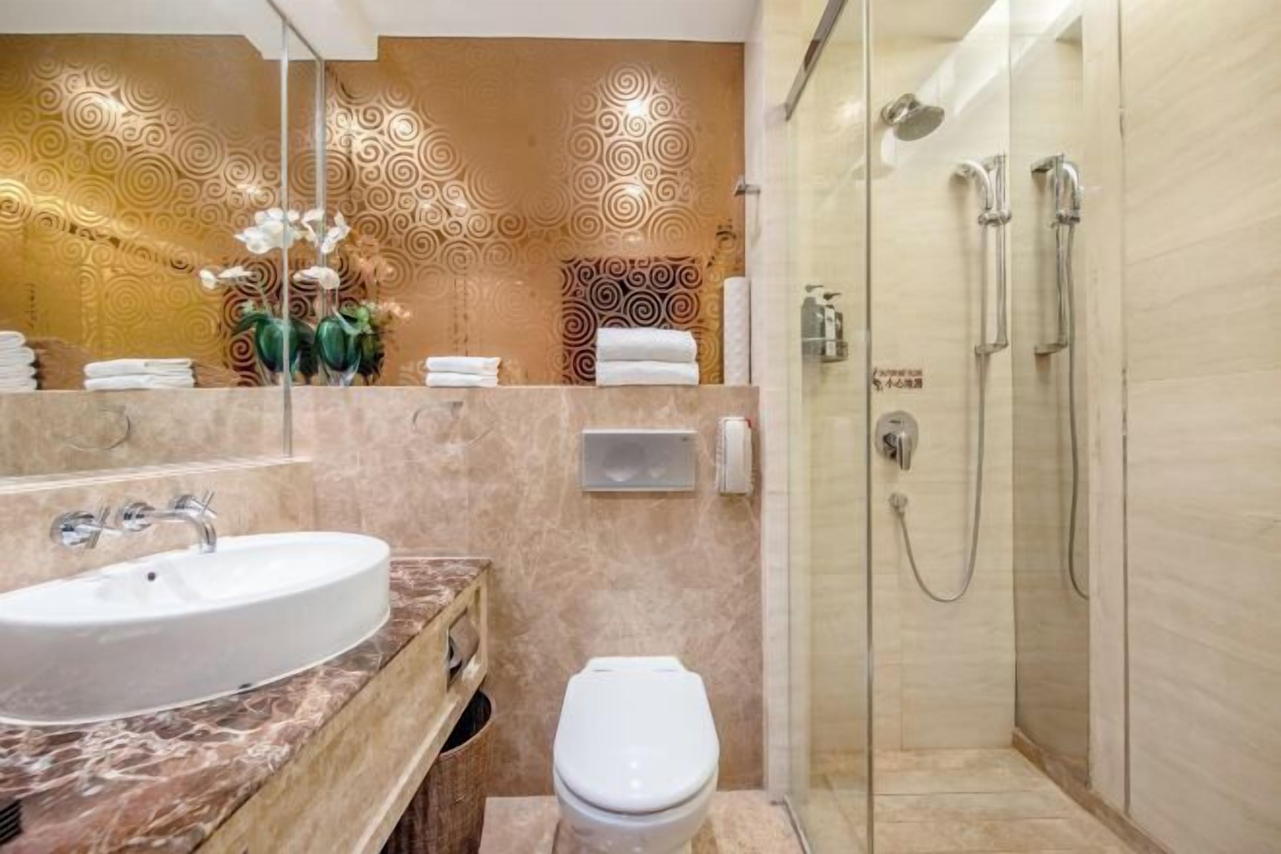 A bathroom with a marble sink, a toilet, a glass shower enclosure, and patterned wall decor.