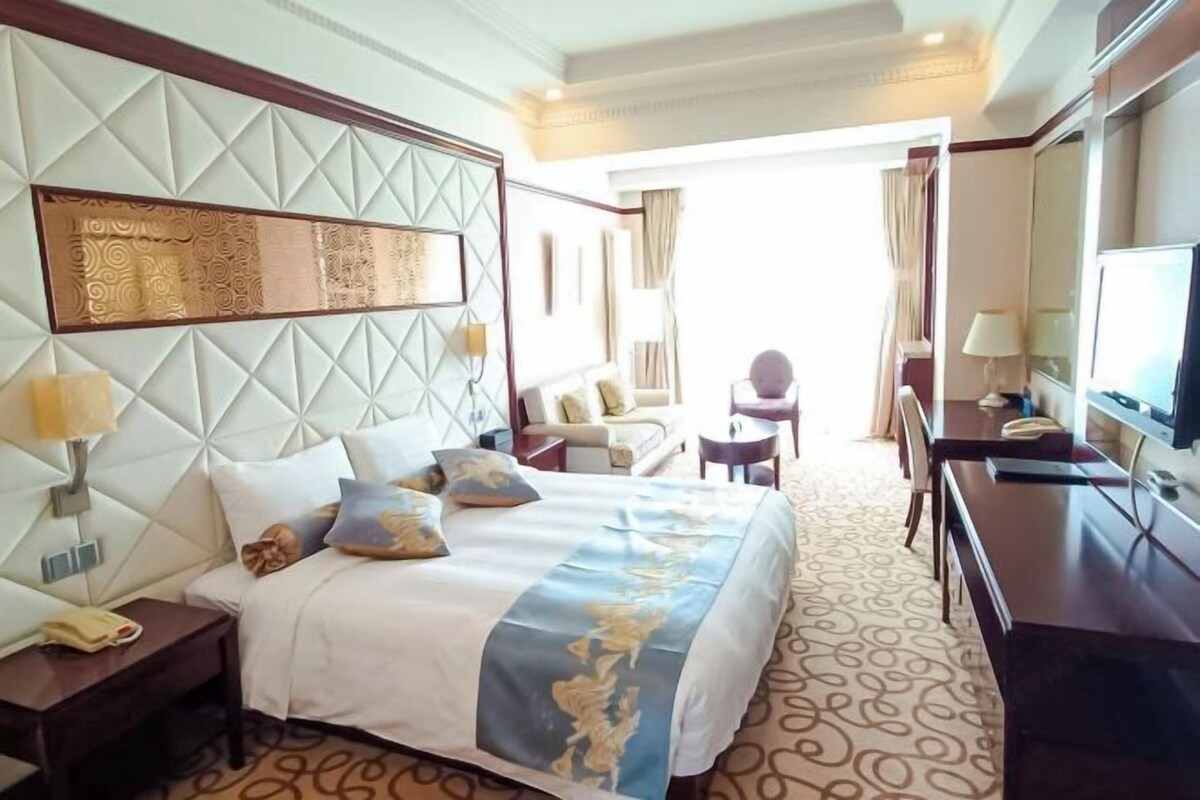 A hotel room with a large bed, a TV, a desk, and a seating area.